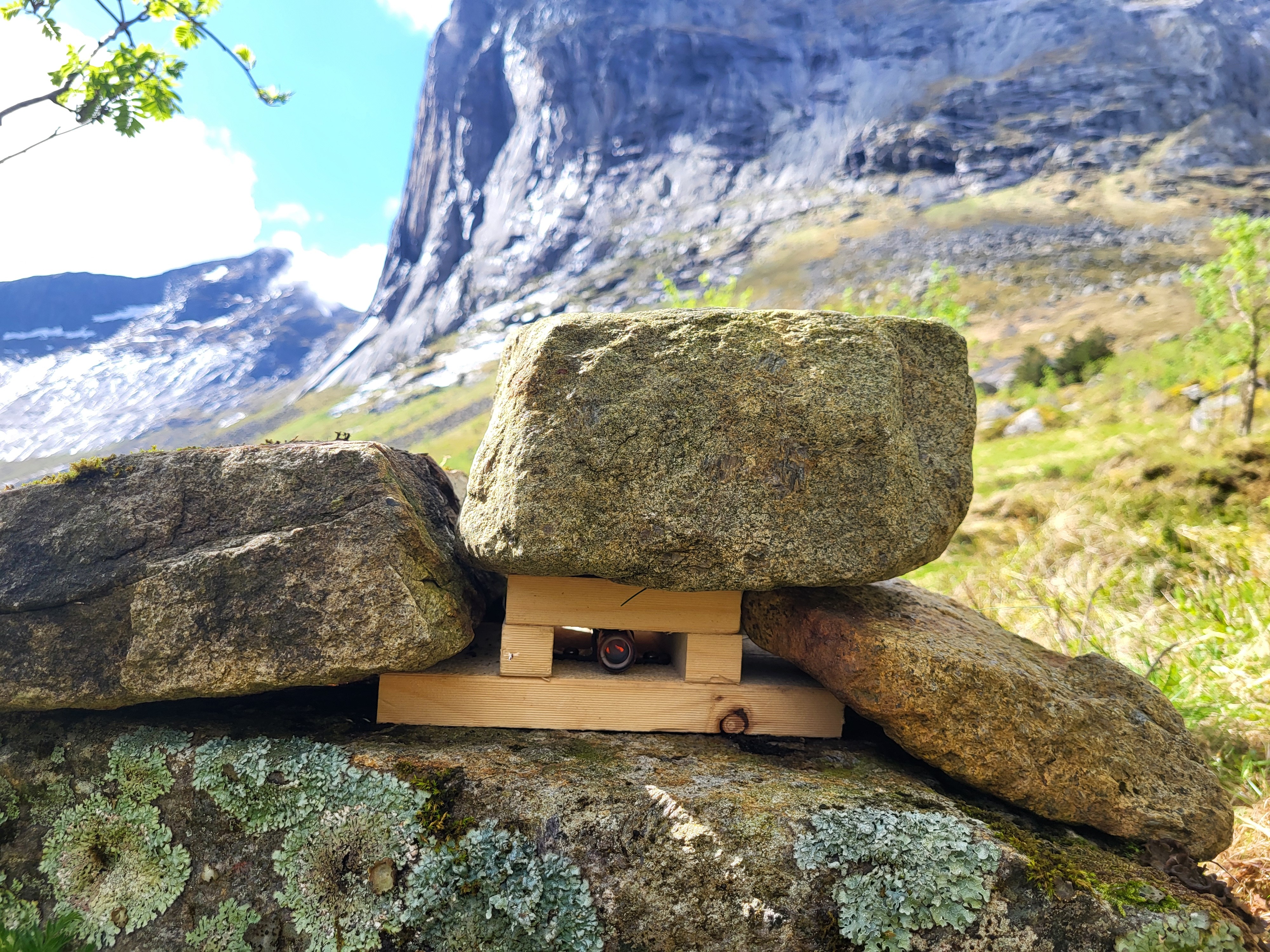 en liten linse gjemt i en steinrøys eller varde. linsen er montert på en ferdselsteller og brukes til å registrerer ferdsel langs en sti.