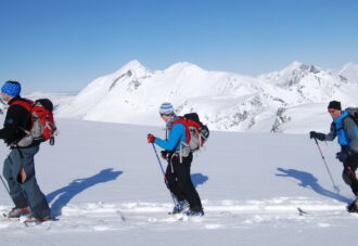 Tre skiløpere (rando) foran alpine fjell