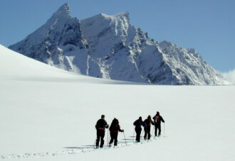 Skiløpere på snøflate foran alpint fjell