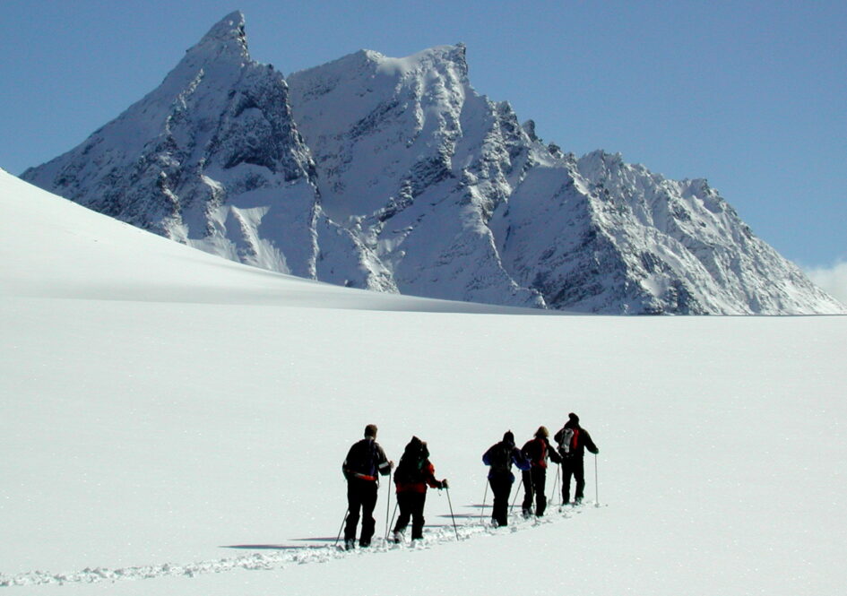 Skiløpere på snøflate foran alpint fjell