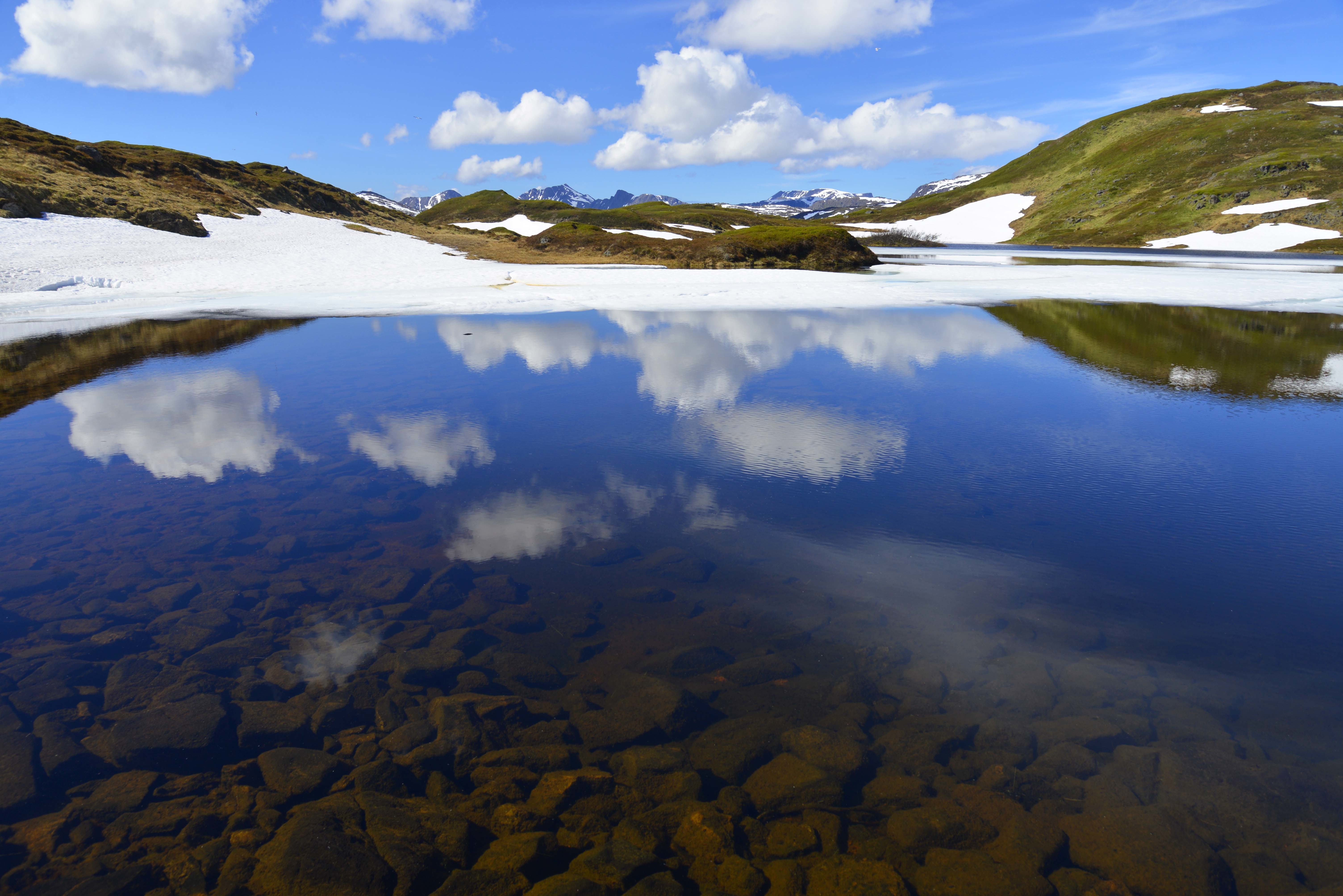 Skyer speiler seg i fjellvann